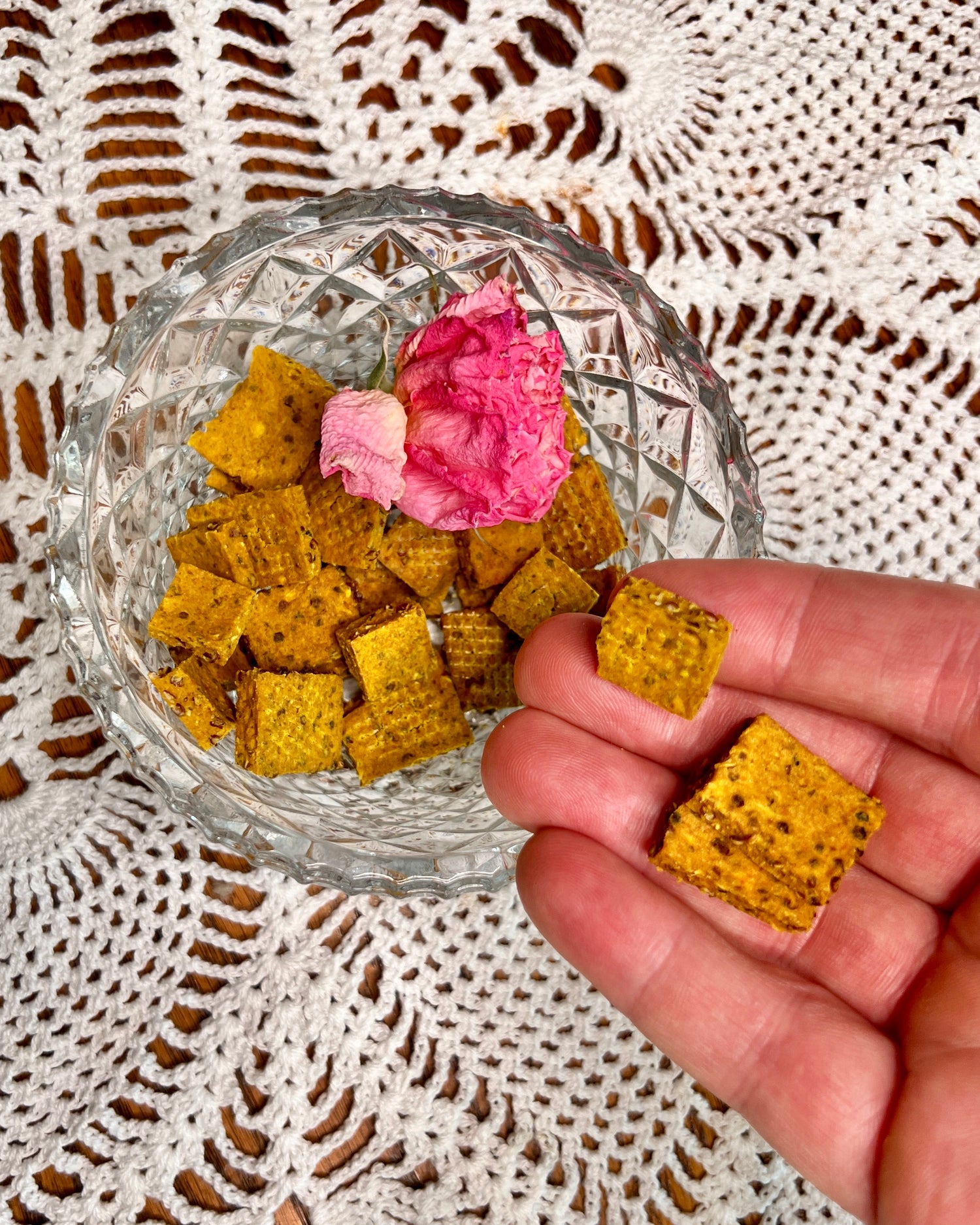 A hand holds a cluster of crunchie tiles over a crystal Bowl.