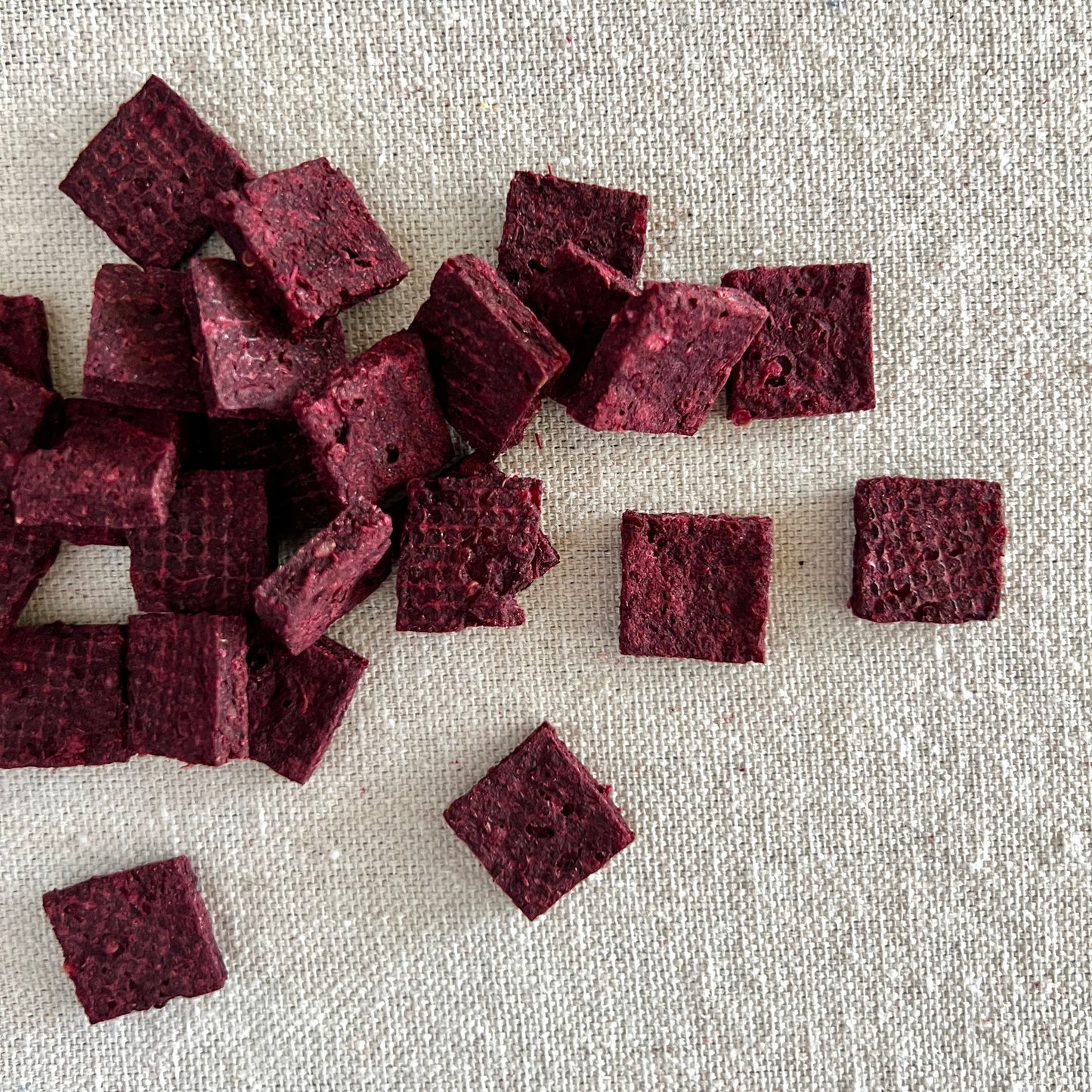 Square purple beet based dog treats on a textured beige surface