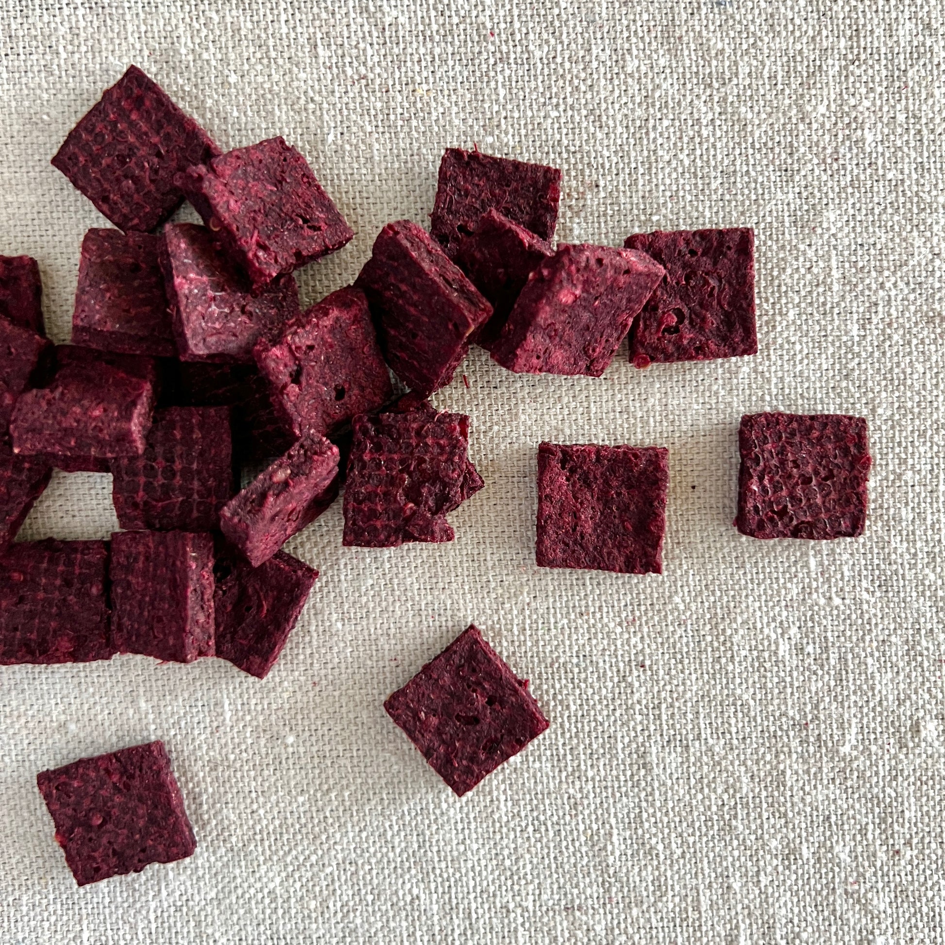 Square purple beet based dog treats on a textured beige surface