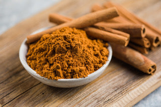 cinnamon powder with cinnamon sticks in a white bowl on a table