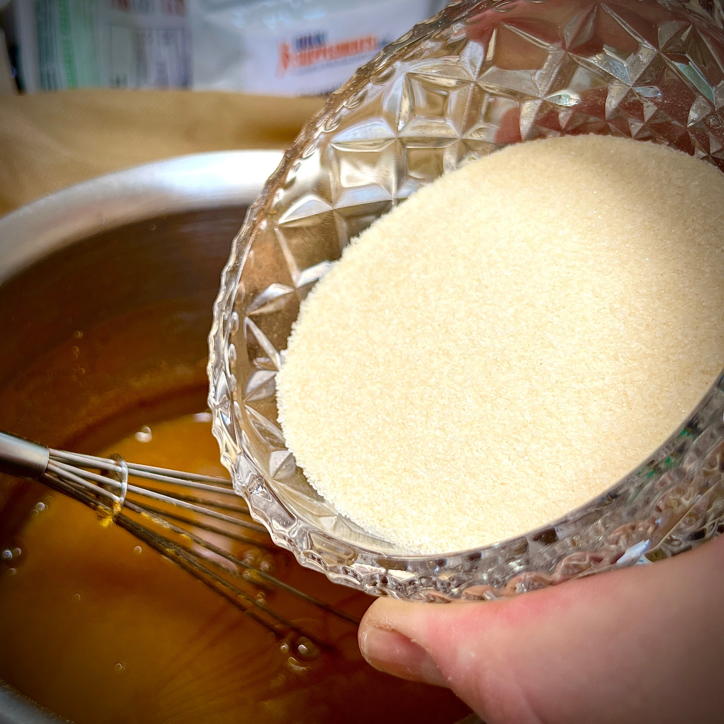 Glass bowl with collagen powder held over a pot with spices, water and a whisk.