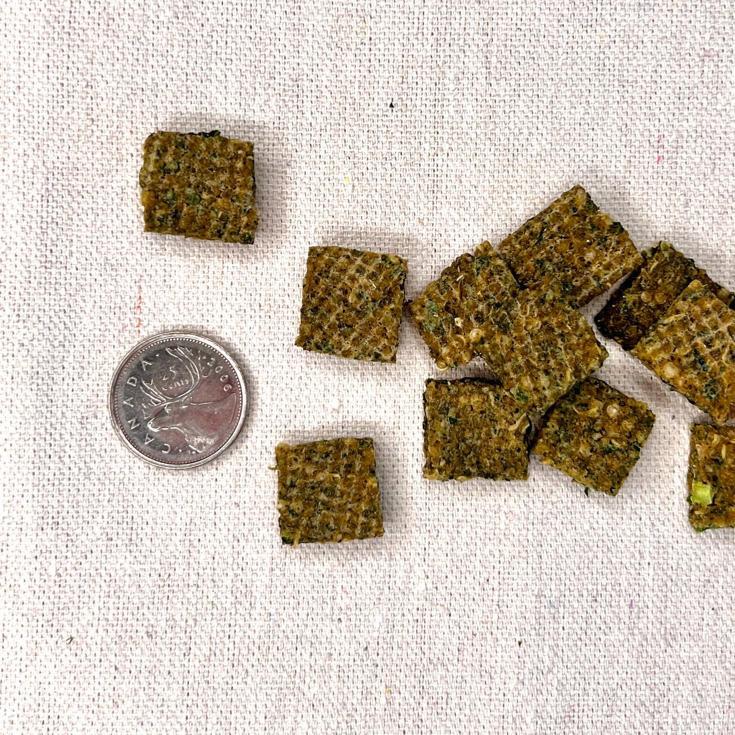 Small square snacks on a textured fabric surface with a coin for scale.