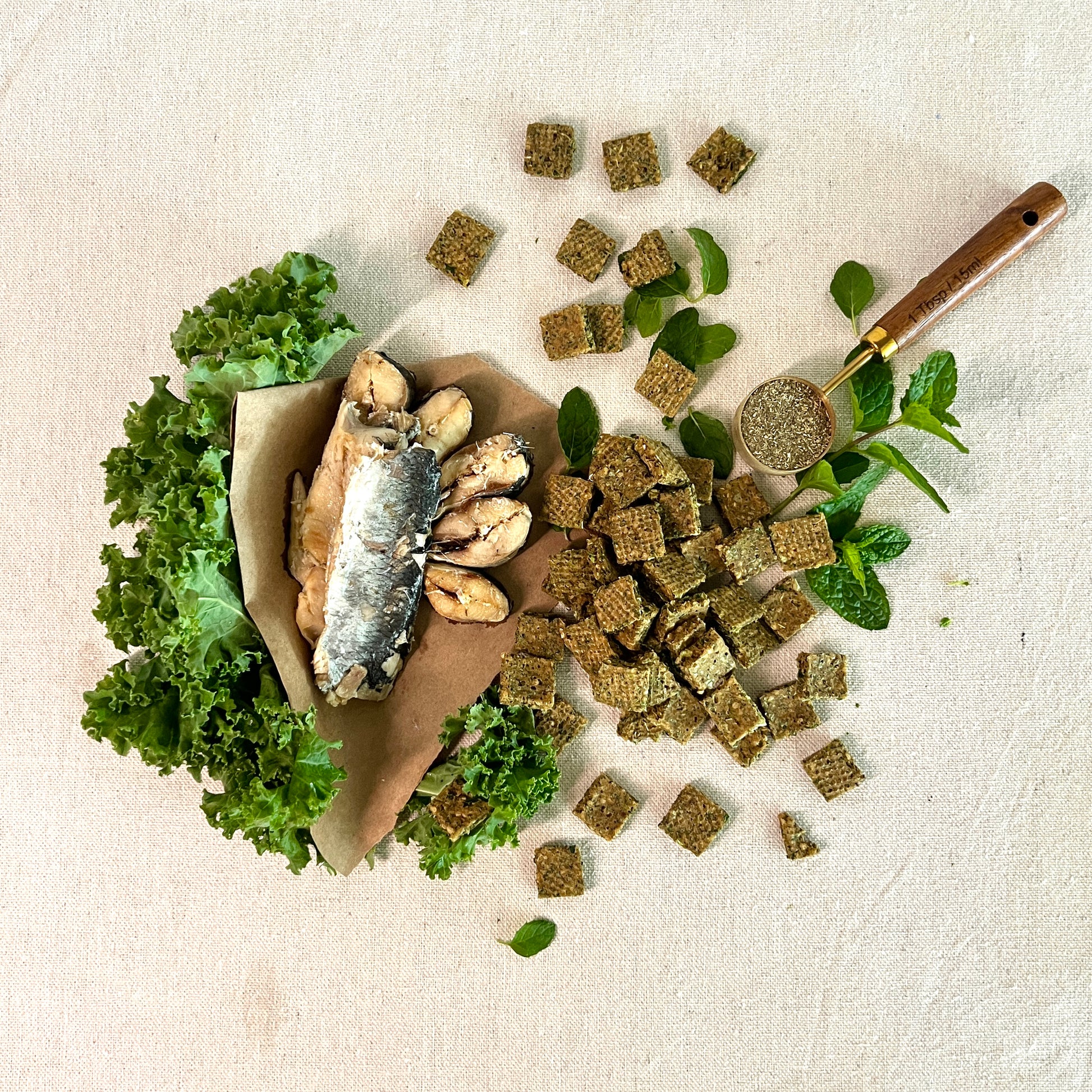 Dried fish with green leaves and a wooden spoon on a textured surface